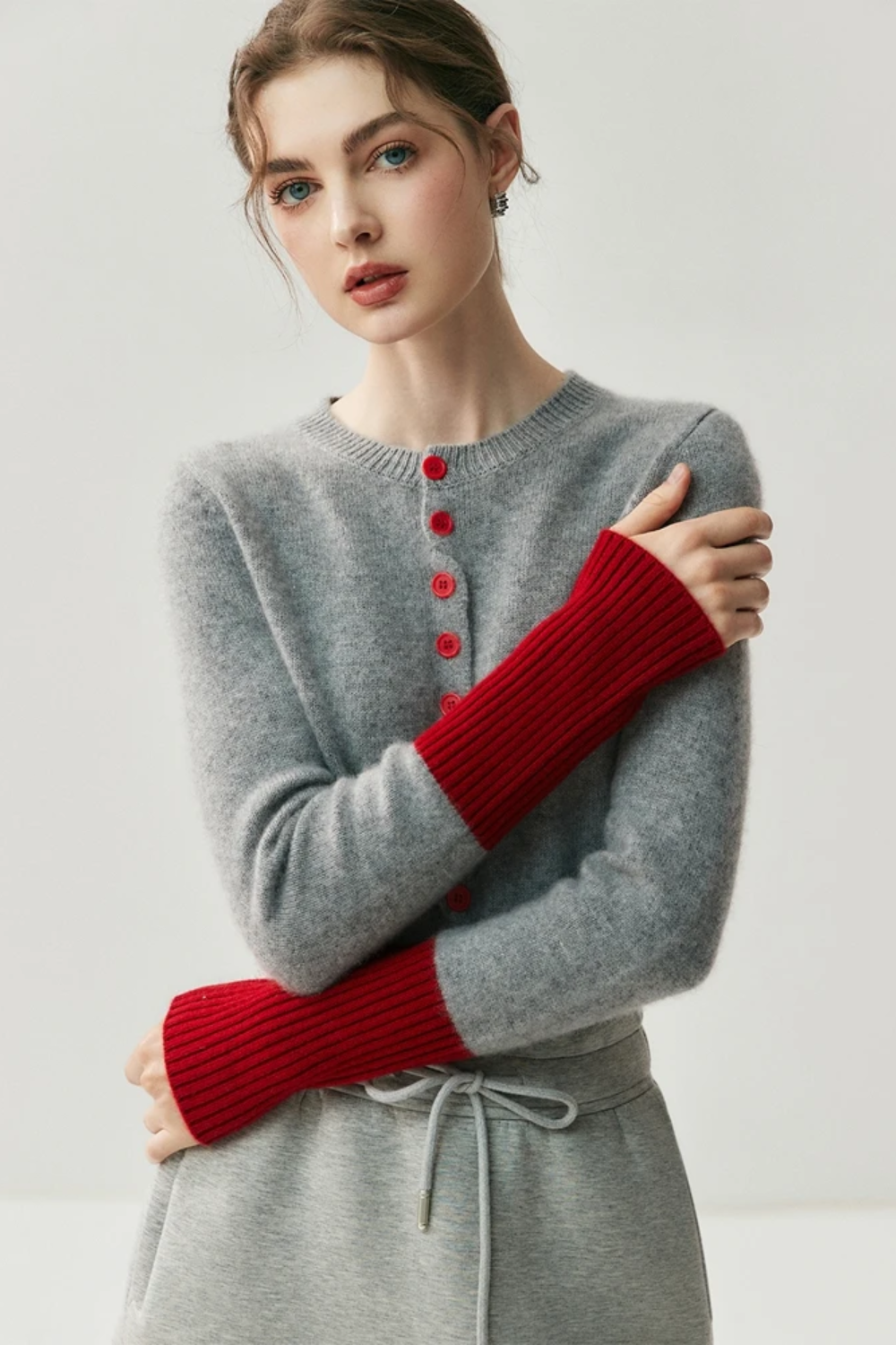 Woman wearing a gray cardigan with red buttons and red sleeves on a light background