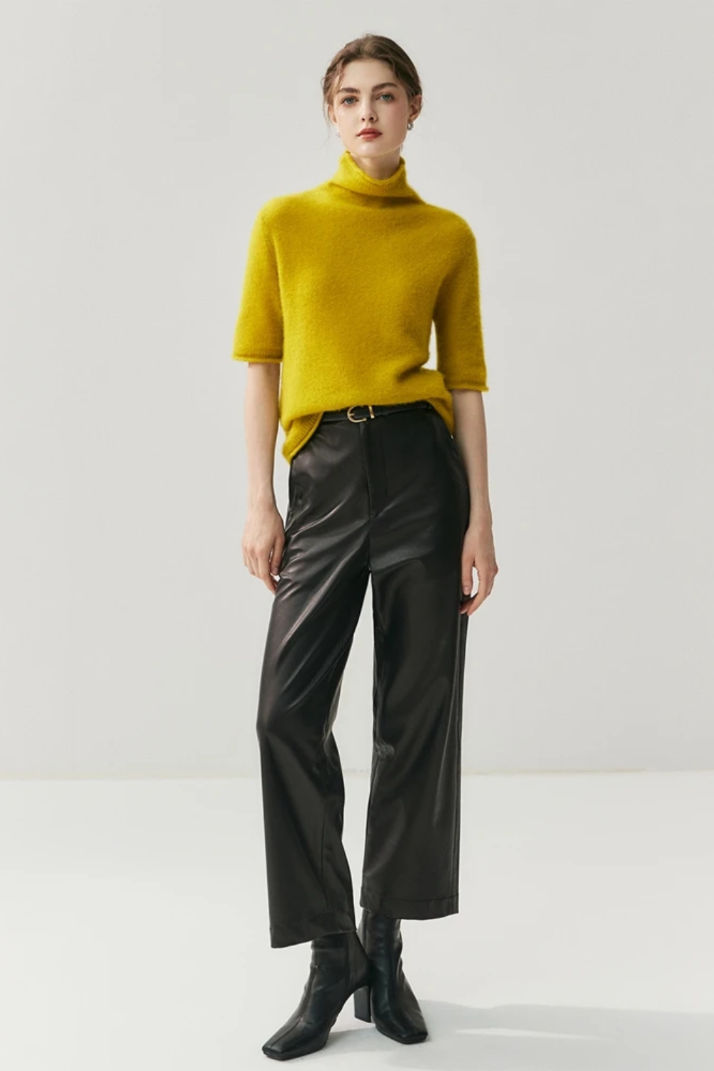 Person wearing a mustard yellow sweater and black pants on a white background