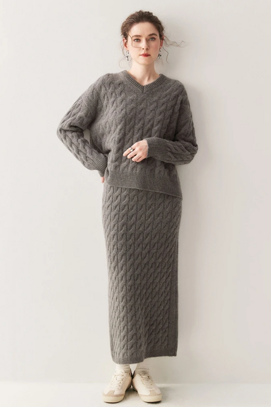 Woman wearing a grey cable knit sweater and ankle length skirt.