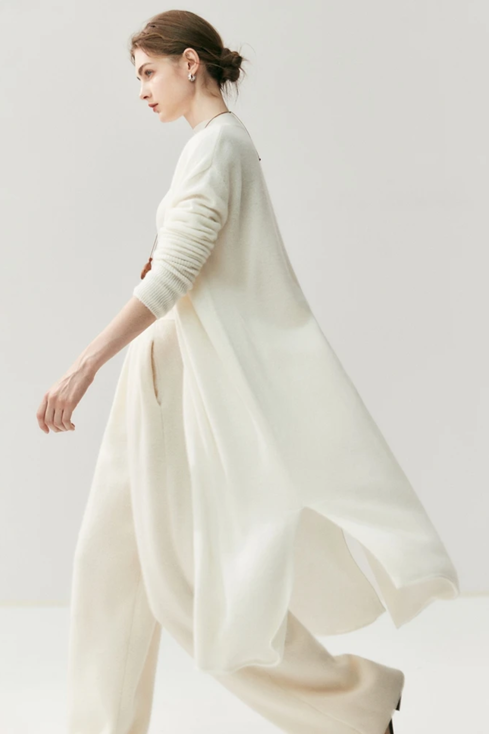 Woman wearing a white outfit with a ahite long cardigan on a white background