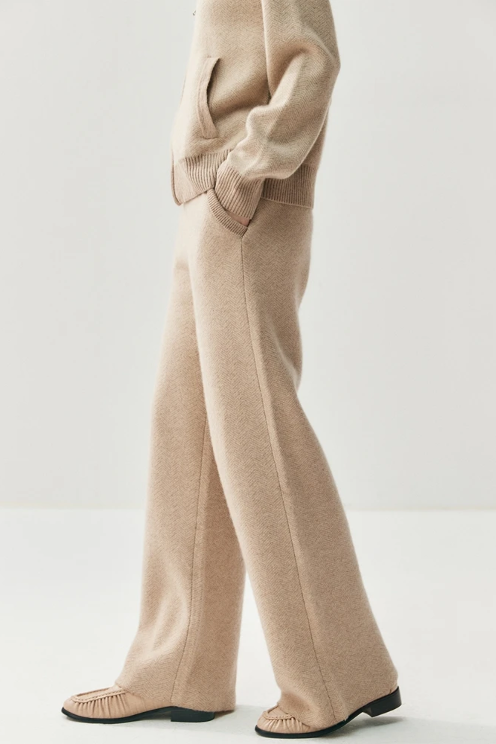 Person wearing a beige sweater and pants on a white background