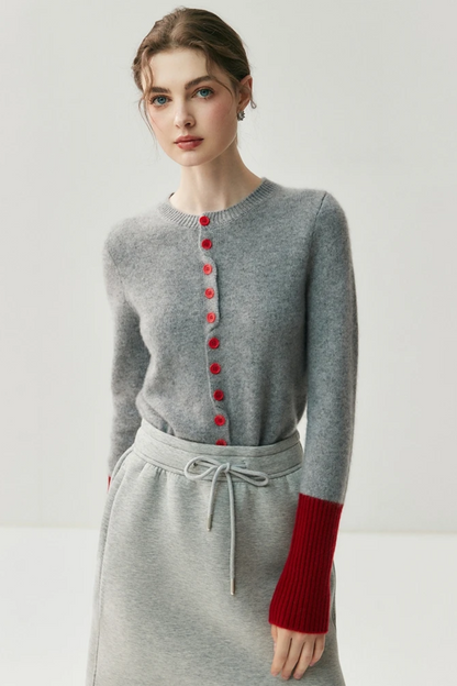 Woman wearing a gray cardigan with red buttons and red sleeves on a light background