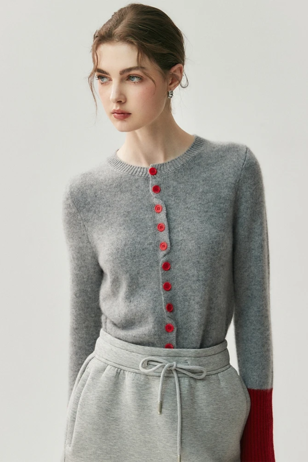 Woman wearing a gray cardigan with red buttons and red sleeves on a light background