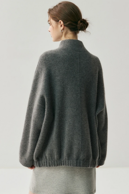 Woman wearing a gray cardigan with a scarf with her back turned on a white background