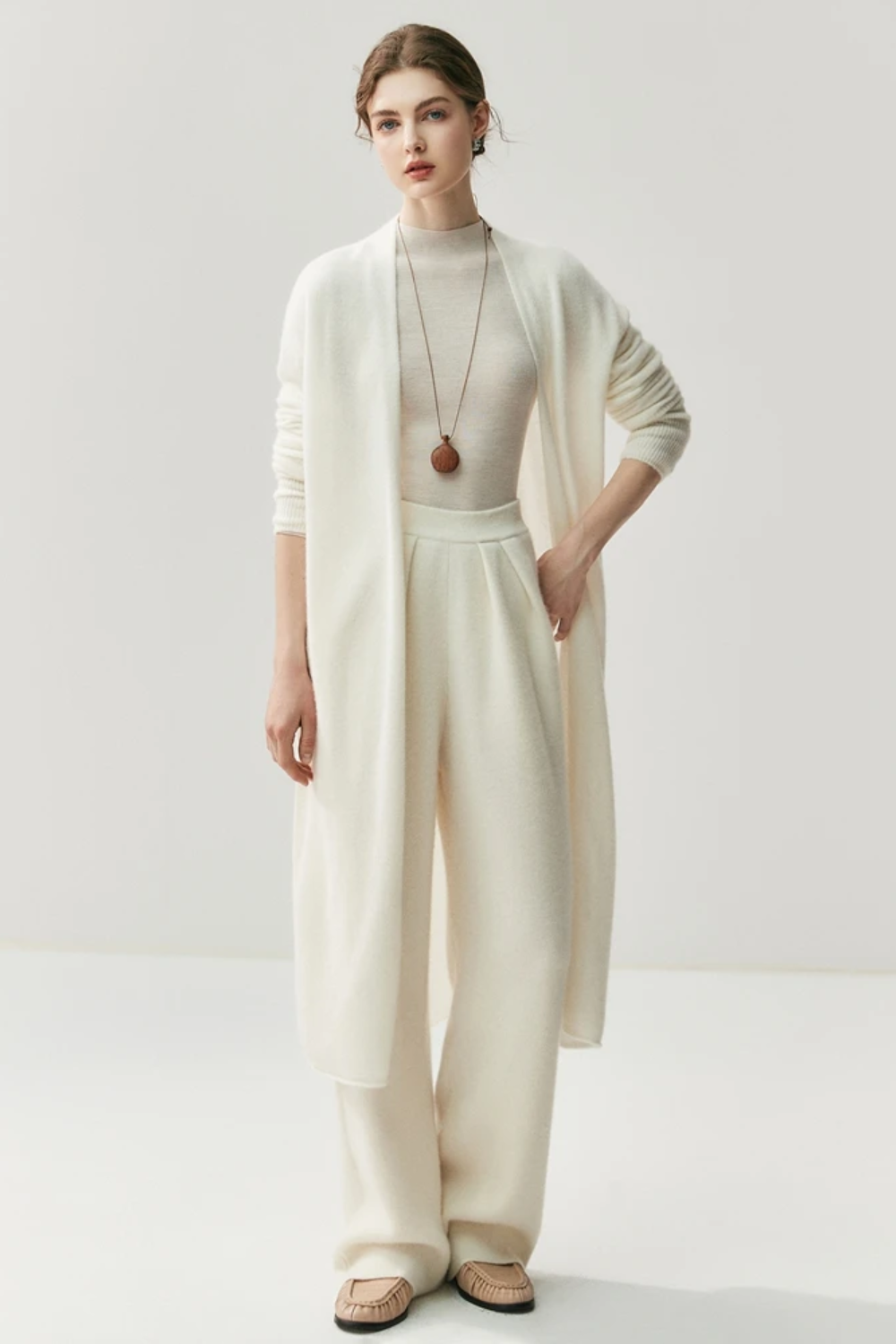 Woman wearing a white outfit with a ahite long cardigan on a white background