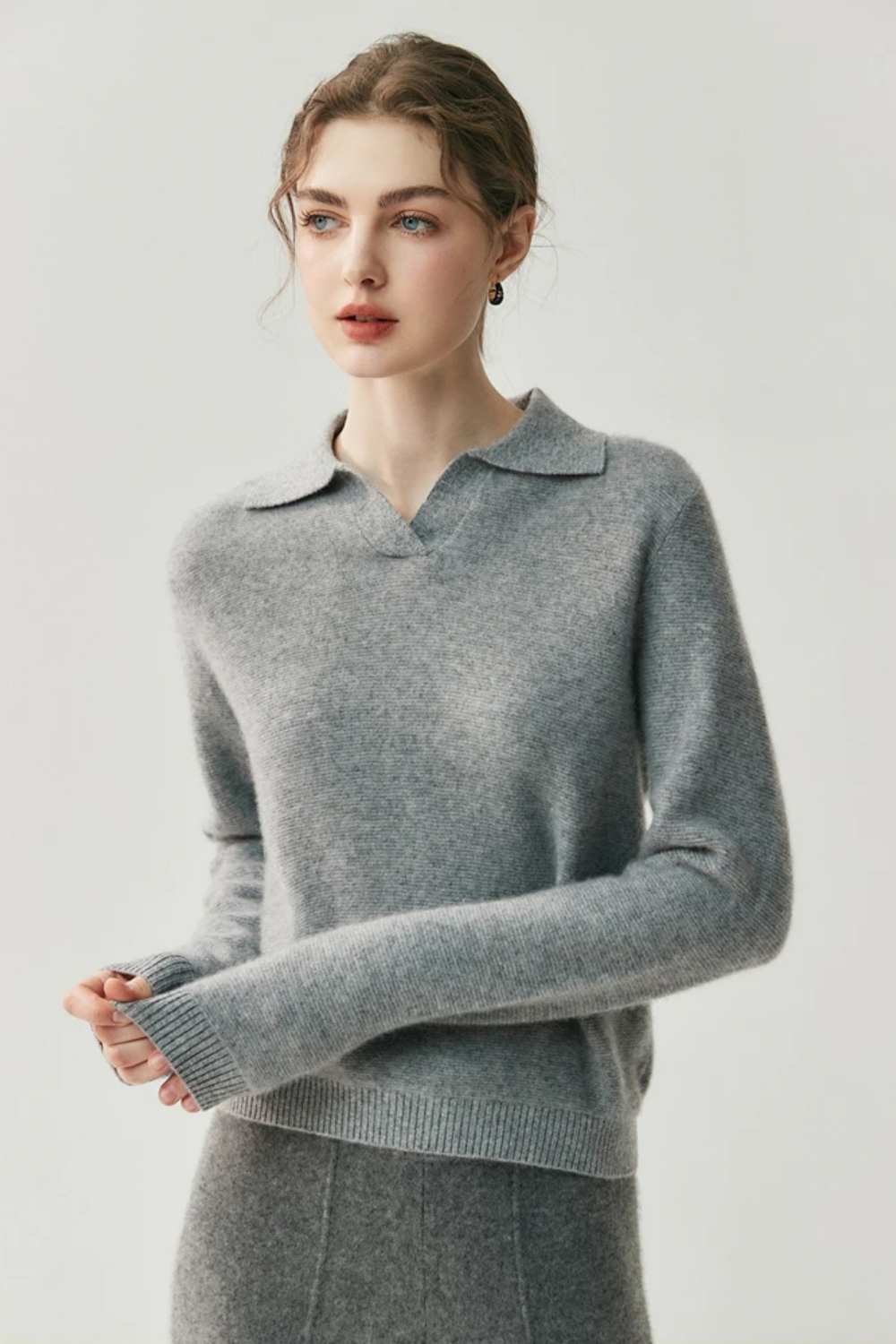 Woman wearing a gray collared sweater and pants against a white background