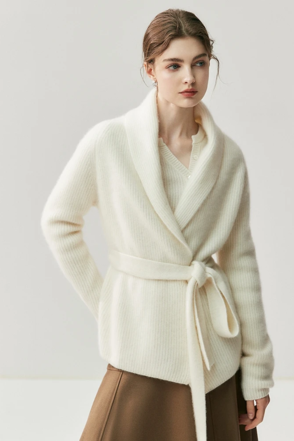 Woman wearing a white cardigan, beige blouse, brown skirt, and beige shoes on a white background