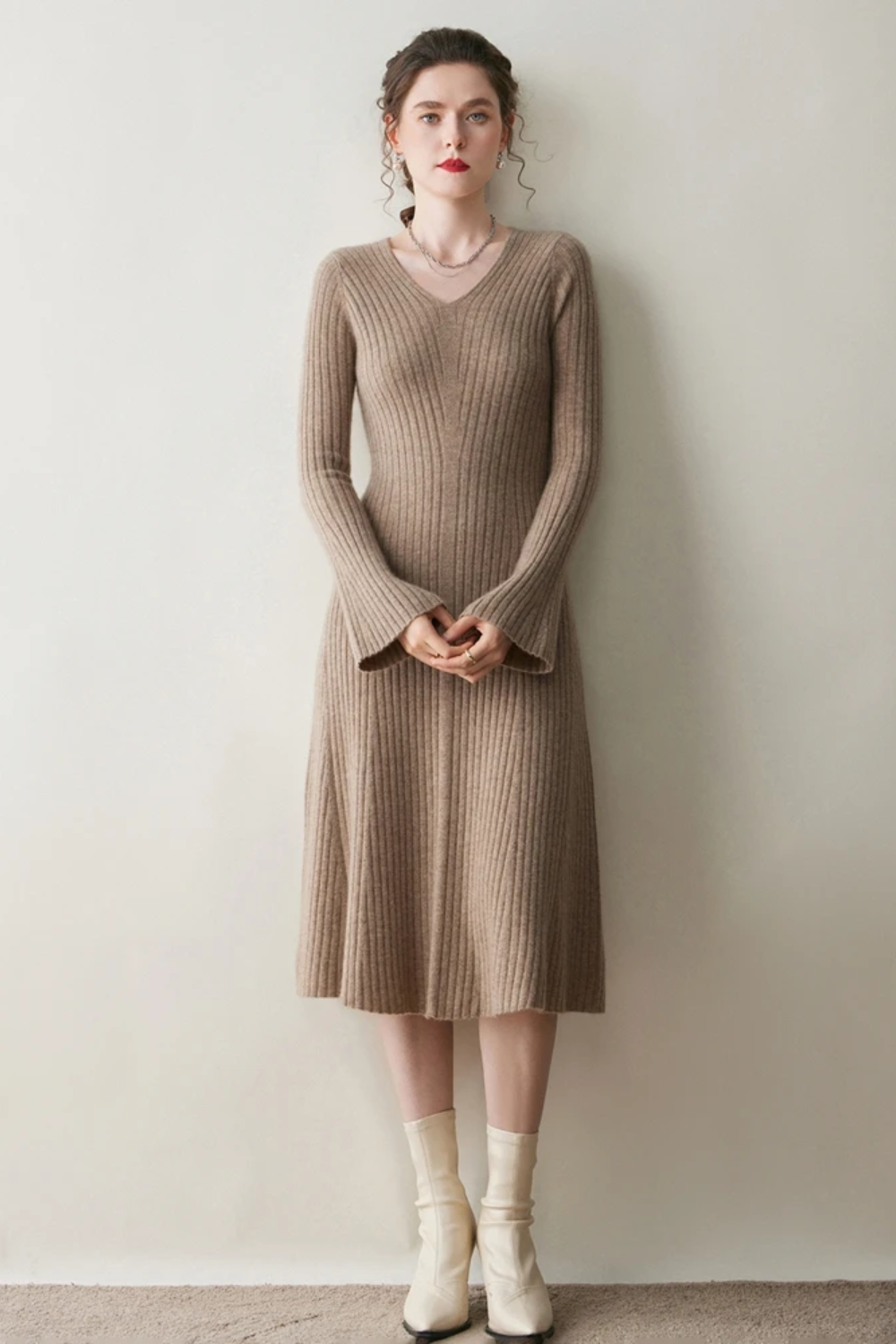 Woman wearing a camel ribbed dress against a plain wall